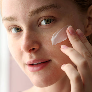 Woman using a white cream from Bioelements skincare on her face.